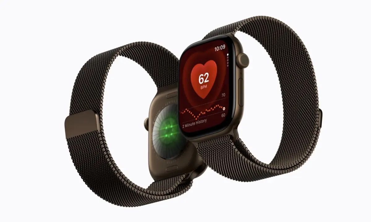Dos Apple Watch Series 12 con correa milanesa: uno muestra el sensor óptico con luz verde por detrás y el otro un ritmo de 62 pulsaciones por minuto en pantalla